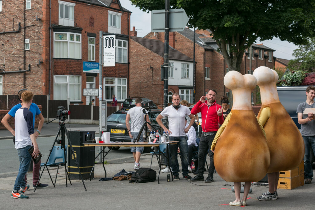 Unit stills photography on location in Manchester. Two people are dressed as chicken drumsticks while film crew look on